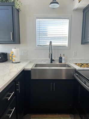 A kitchen with a stainless steel sink, dark cabinets, a window with blinds, and a marble countertop. - The Sunflower Villa - 15 Miles from the Beach! (Foley)