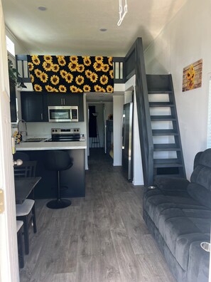 A compact kitchen with modern appliances, a dining area with a bar stool, and a staircase leading to an upper level. - The Sunflower Villa - 15 Miles from the Beach! (Foley)