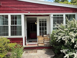 A red house with a white door, large windows, and a small porch with wooden steps.