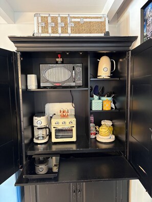 Eine kompakte Küche mit Mikrowelle, Toaster, Kaffeemaschine und Wasserkocher.