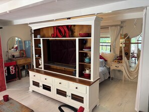 A room with a white cabinet with drawers, a mirror, a red 'JOY' sign, and a hammock.