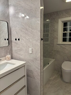 A modern bathroom with a marble floor, a glass shower enclosure, a white sink, and a toilet. - Hamptons Retreat Pool Oasis Modern House (Hampton Bays)