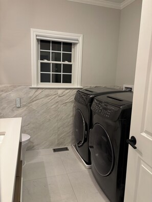 A laundry room with two front-loading washers, a window above the sink, and a white door. - Hamptons Retreat Pool Oasis Modern House (Hampton Bays)