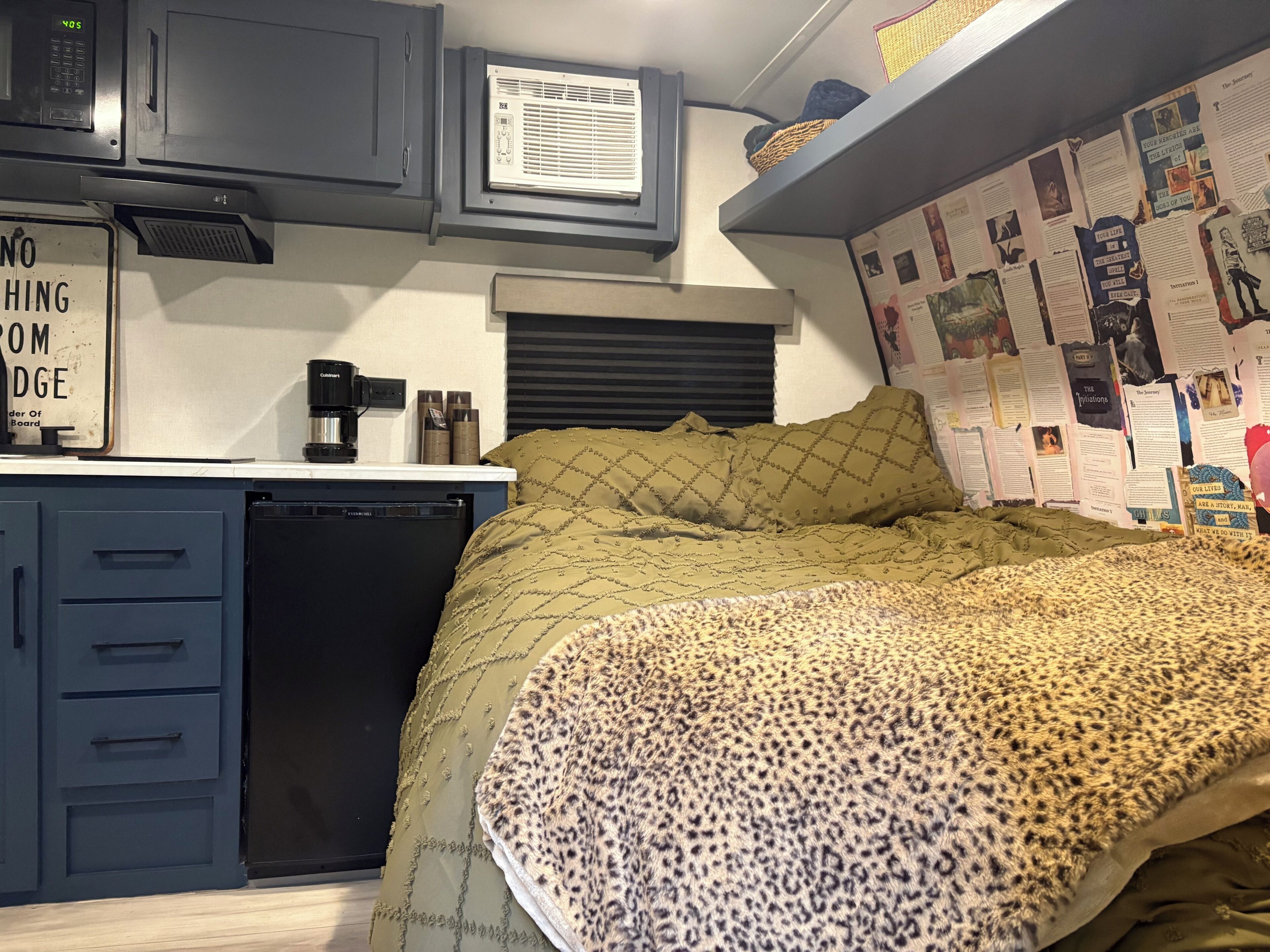 A compact bedroom with a bed, a small desk with a coffee maker, a microwave, and a refrigerator.