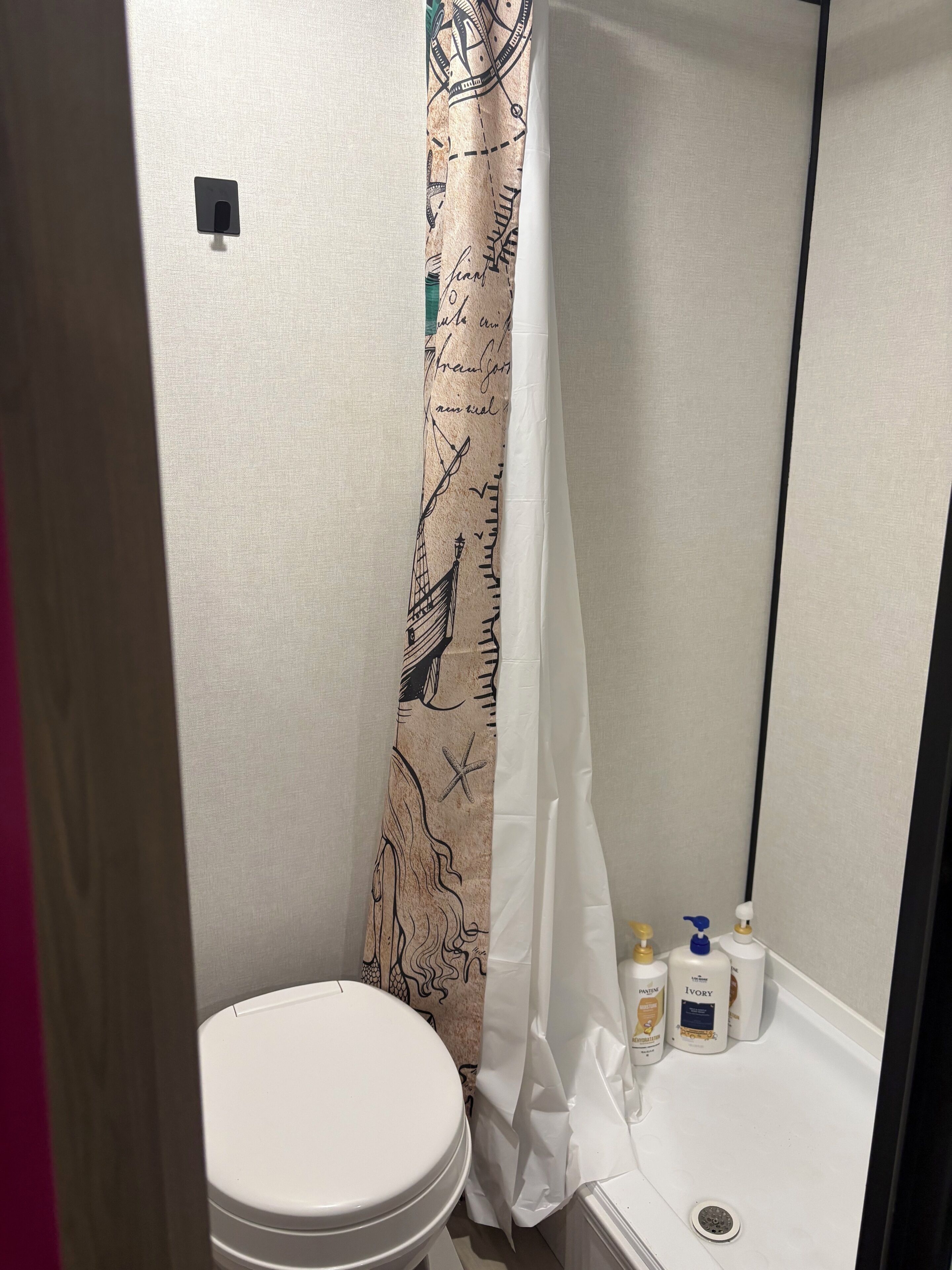 Ein Badezimmer mit Toilette, einer Duschkabine mit Meeresmotiv und Pflegeprodukten am Waschbecken.