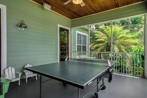 A ping pong table on a porch with chairs, a door, and a view of greenery. - Lakefront Getaway on Lake June — Sleeps 12 (Lake Placid)