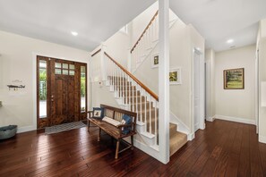 A spacious foyer with a wooden bench, a staircase with white railings, and a large wooden door. - Lakefront Getaway on Lake June — Sleeps 12 (Lake Placid)