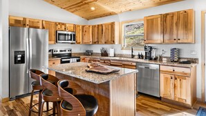 A modern kitchen with wooden cabinets, stainless steel appliances, and a central island with bar stools. - NEW CABIN-Epic Sunsets! Panoramic Views of Blue Ridge and Smokey Mountains! (Murphy)