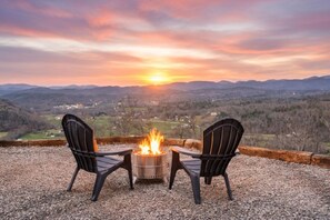 Feuerstelle mit zwei Stühlen und Blick auf einen Sonnenuntergang über einem Tal.
