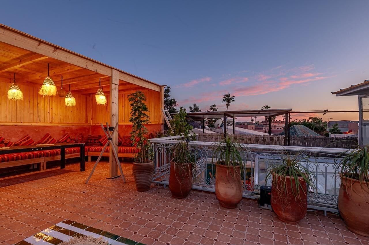 Terraza en la azotea con asientos de madera, plantas en macetas e iluminación colgante.