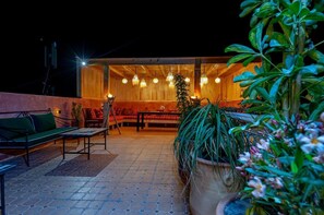 Un área de estar al aire libre con una estructura de madera, múltiples luces colgantes y plantas en macetas.