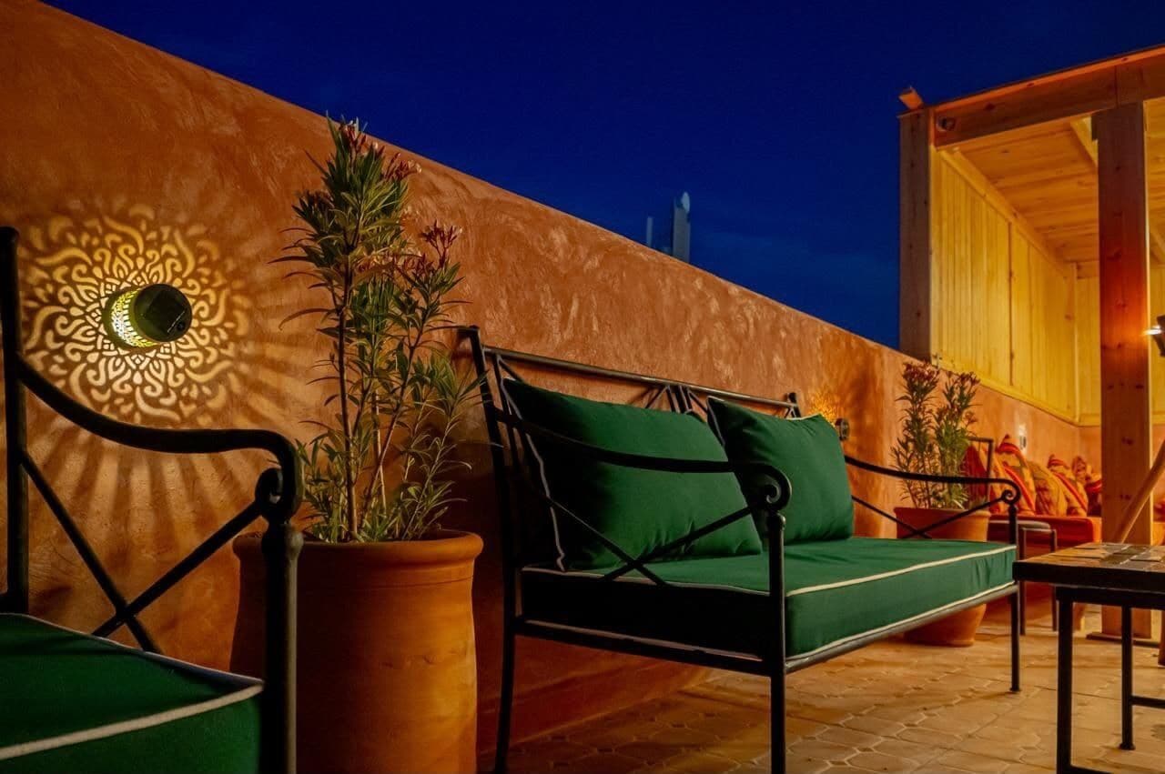 An outdoor seating area with a sofa and chairs, potted plants, and a decorative wall with a geometric pattern.