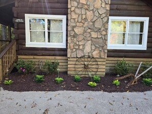 Una cabaña con dos ventanas, un muro de piedra y una terraza de madera.