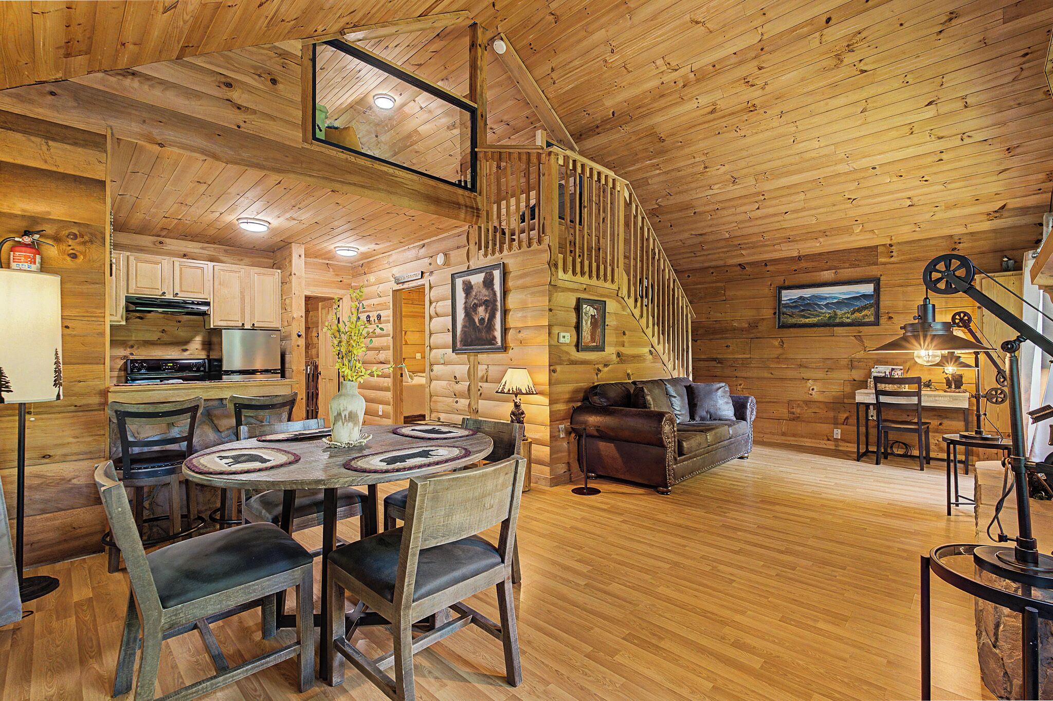 A log cabin interior with a dining area, a sofa, a staircase, and a kitchen.