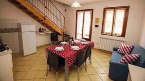 Een eethoek met een tafel voor vier personen, een keuken met een koelkast, een blauwe bank en een houten trap.