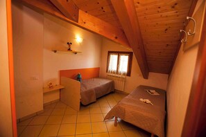 A small, cozy room with two single beds, a shelf with a decorative item, a window with curtains, and a wooden ceiling. - Holiday apartment with pool (Rosolina Mare)