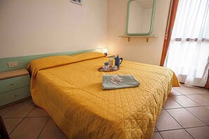 A hotel room with a bed, a bedside table, a mirror, and a window with curtains. - Holiday apartment with air conditioning (Rosolina Mare)