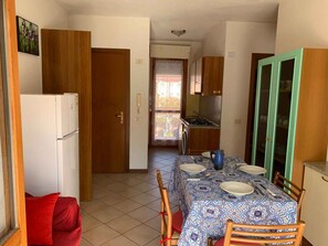A compact kitchen with a refrigerator, a dining table set for four, and a small window with a view. - Holiday apartment with air conditioning (Rosolina Mare)