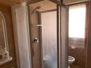 A shower enclosure with a glass door, a handheld showerhead, and a toilet visible in the adjacent room. - Holiday apartment with air conditioning (Rosolina Mare)