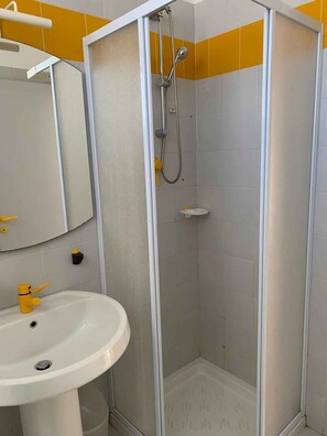 A bathroom with a white sink, a mirror, a shower with a glass door, and yellow tiles on the wall. - Holiday apartment in a residence with pool (Rosolina Mare)