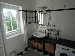 Ein Badezimmer mit Fenster, Waschbecken, Spiegel, Waschmaschine und Körben aus Weidwerk.