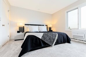 Un dormitorio moderno con cama, lámparas de noche, una ventana y un equipo de aire acondicionado.