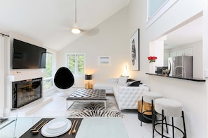 A modern living room with a fireplace, a flat-screen TV, a sofa, and a dining area with a table set for two. - ⛳ Hilltop 3BR Condo | Bay Views + Golf | Near GT Resort | Adults 25+ (Acme)