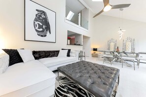 Una sala de estar moderna con un sofá blanco, un reposapiés de cuero y una obra de arte grande enmarcada.