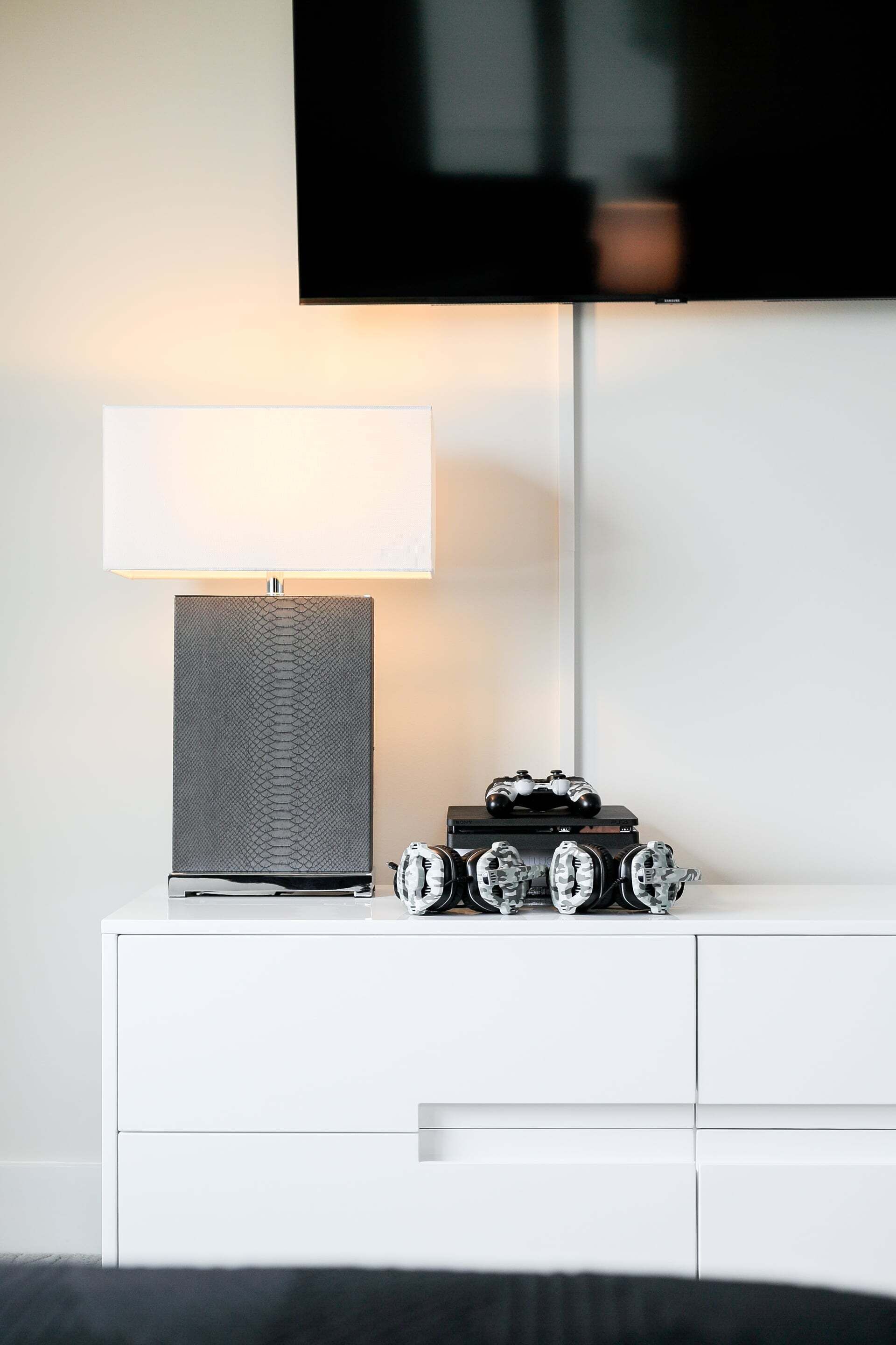 A white bedside table with a lamp, a flat-screen TV, and vintage cameras.