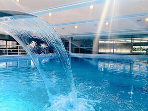 Piscina con cascada, iluminación interior y un diseño arquitectónico moderno.
