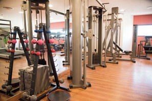 Uma academia com diversos equipamentos de exercício, piso de madeira e espelho.