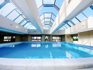 Una piscina interior con tragaluces, agua azul cristalina y vistas de la ciudad.