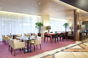 Een hotellobby met een eetgedeelte, grote ramen en een centrale kolom.