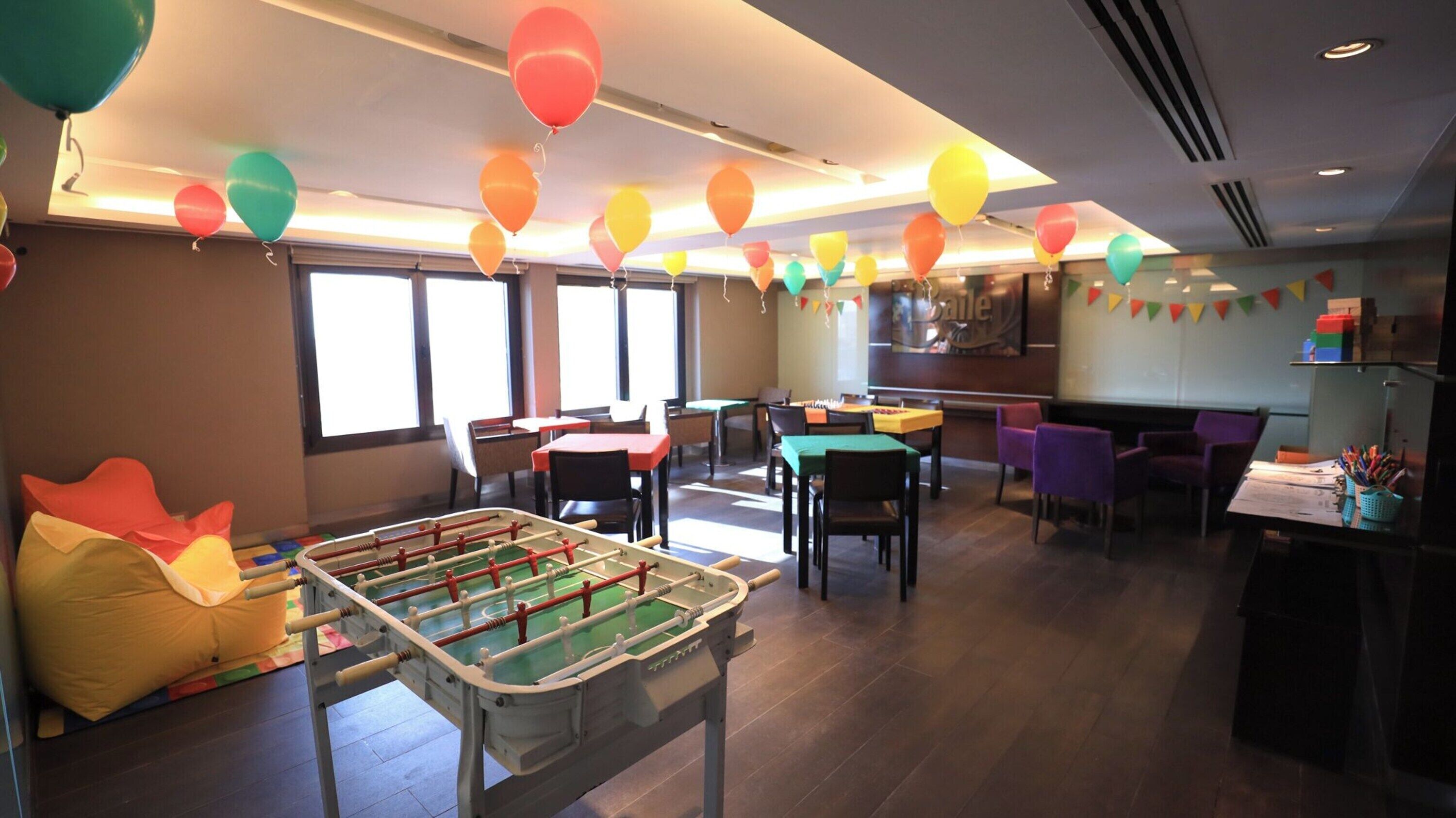 Une pièce avec un baby-foot, des tables, des chaises et des ballons de couleurs vives.