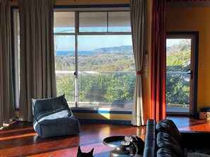A room with a large sliding glass door to a balcony, a black leather sofa, a blue bean bag chair, and a small table with a decorative item.