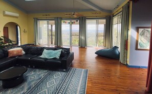 A living room with a black leather sofa, a patterned rug, and a view through large glass doors.