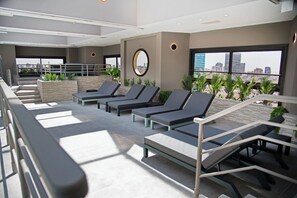 Um lounge no terraço com espreguiçadeiras, uma janela circular e vista para a cidade.