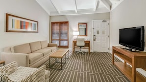 Habitación de hotel con sofá, escritorio, televisor y alfombra estampada.