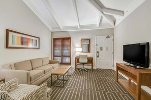 A hotel room with a sofa, a desk, a television, and a patterned carpet.