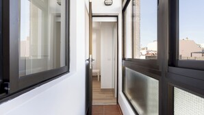 A corridor with a door leading to a room, a window with a view of buildings, and a ceiling light fixture.