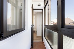 Ein Korridor mit einer zur Zimmerführenden Tür, einem Fenster mit Blick auf Gebäude und einer Deckenleuchte.