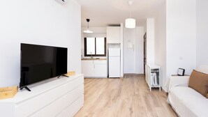 A modern living room with a flat-screen TV, a sofa, and a dining area with a kitchen in the background.