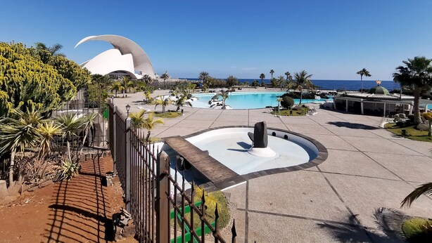 A resort with a large pool, a cactus garden, and a distinctive white building with a curved roof.