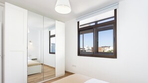 A bedroom with a bed, a window, a mirror, and a wardrobe.
