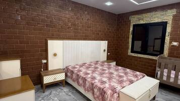 Un dormitorio con pared de ladrillo, una cama con colcha estampada, una mesita de noche, un aparador y una ventana con vistas.