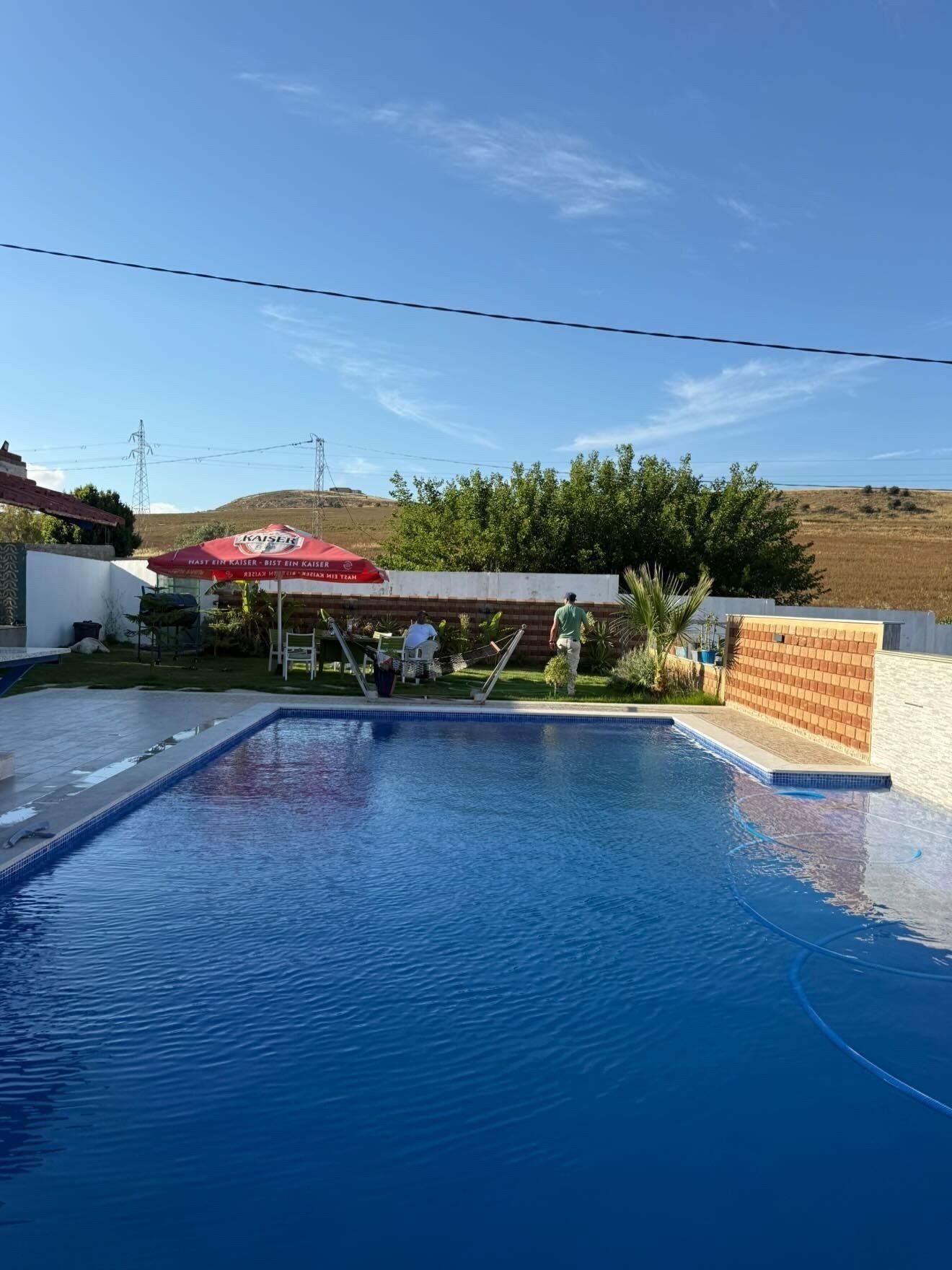 Una piscina con superficie de agua azul cristalina, rodeada por un muro blanco y una estructura de ladrillo.