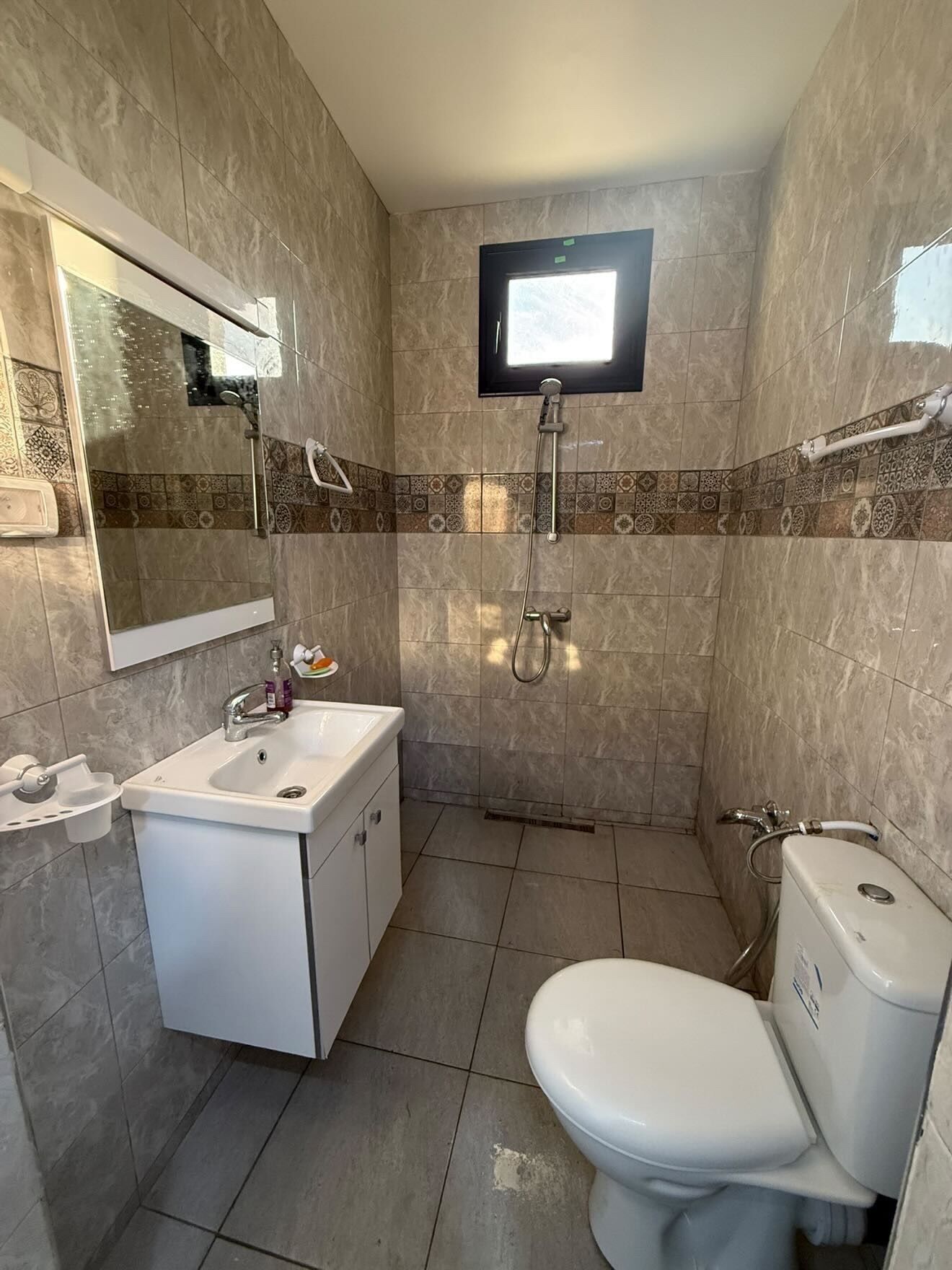 A bathroom with a sink, toilet, shower, and a mounted television.
