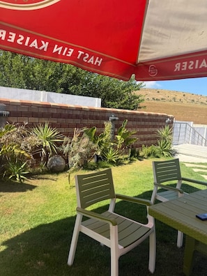 Een terras met twee groene plastic stoelen, een tafel en een rode parasol.