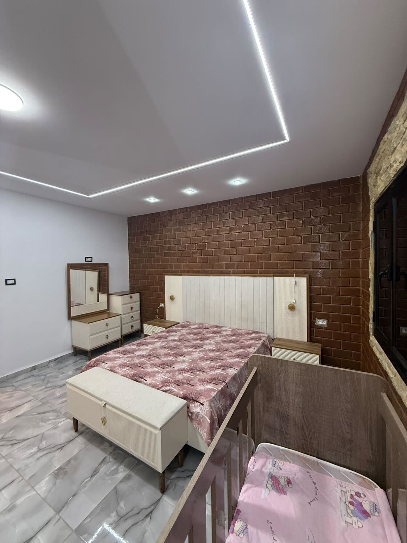 Une chambre à coucher avec un lit, une commode, un miroir et un mur décoré d’un motif en briques.
