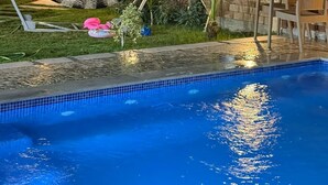 Piscina com borda azulejada, cercada por um muro de tijolos, área gramada e plantas em vasos.